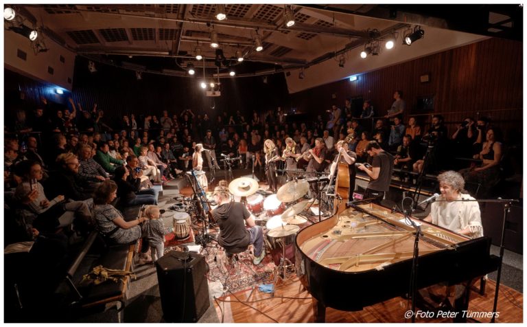 Live Concert of Om Shira & The Exile Orchestra with a Grand Piano and people around the sitting stage